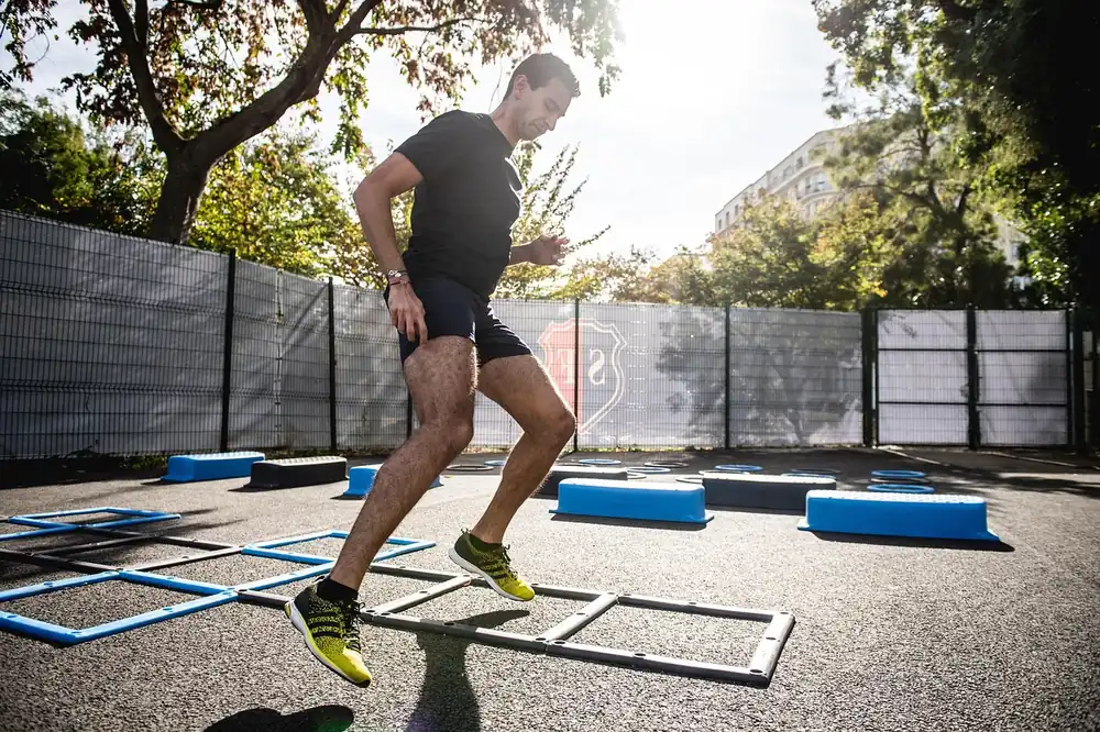 An athlete driving through an agility ladder outdoors